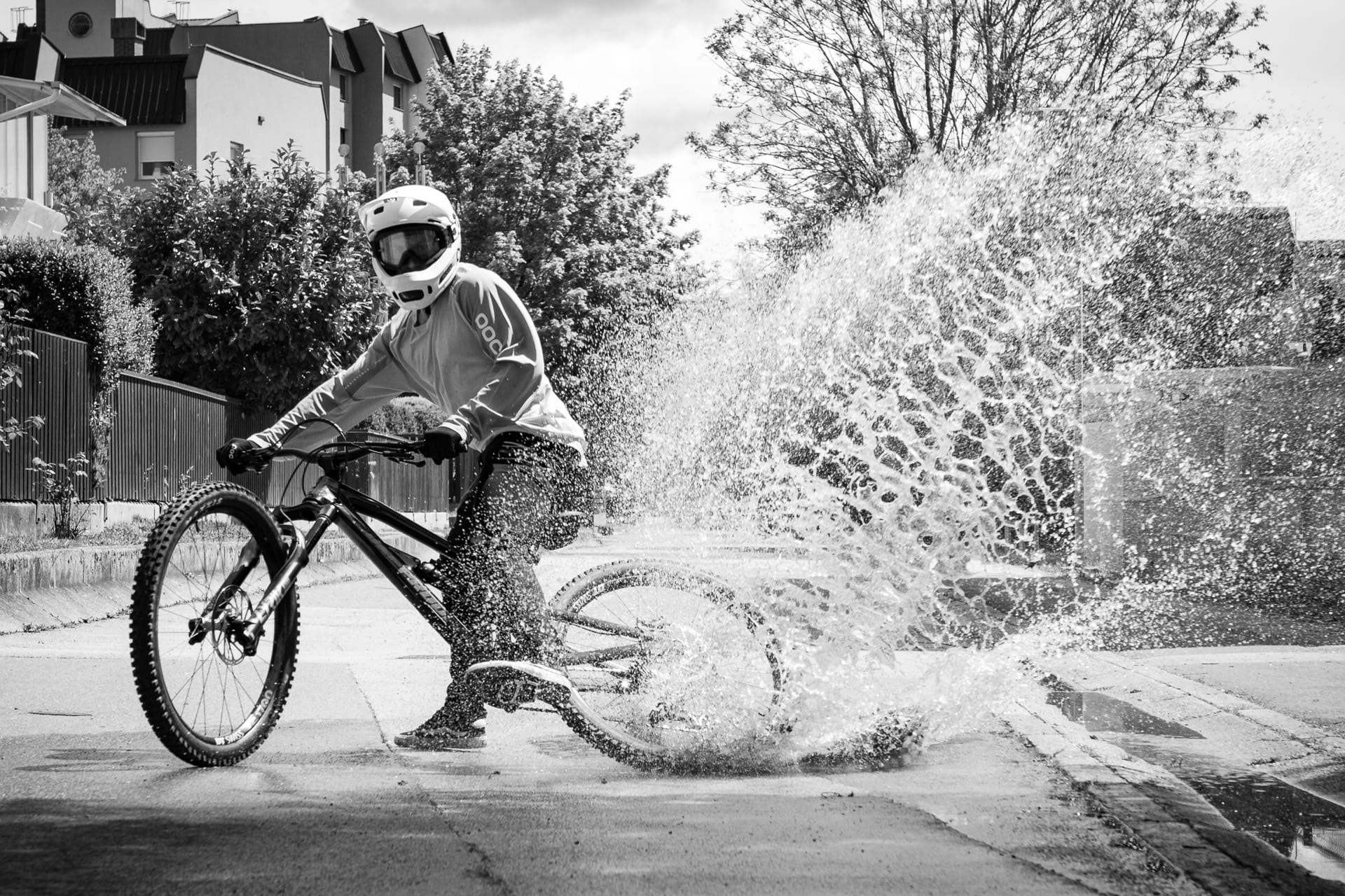 BineZalohar@KeepBusybyLegitFilms©KatjaPokorn Bike rider making splash in big rain puddle on a street among residential buildings
